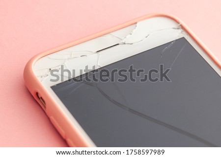 Broken phone with crack on the display glass on pink background.