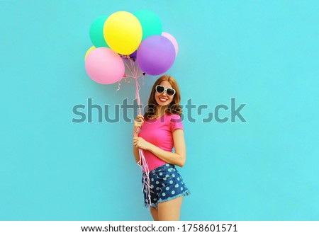 Funny woman with bunch of balloons having fun wearing a shorts and pink t-shirt on blue wall background