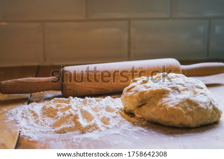 Concept - Baking Bread. Rolling pin, dough, and flour on a wooden surface. Red tones, soft focus. London, UK -Image