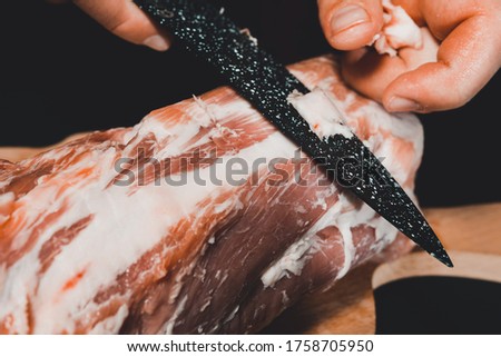 The chef of the restaurant in a dark uniform cuts the meat with a black kitchen knife. Preparation of pork marinated steak to order.