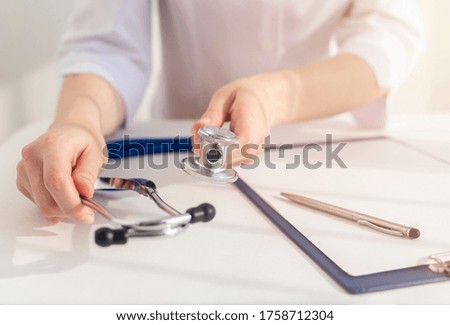 Stethoscope laying on medicine doctor working table with doctor hands taking stethoscope with paper board with pen. Healthcare and medical concept.
