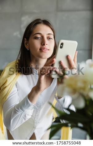 Beautiful lovely brunette woman taking a picture of a flower bouquet while standing at home