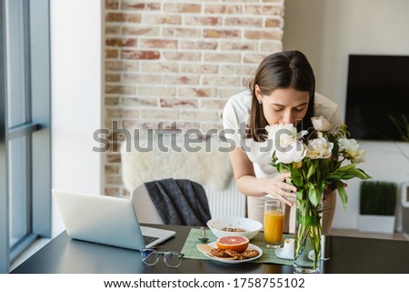 Beautiful lovely brunette woman admires flower bouquet in vase while standing in the kitchen
