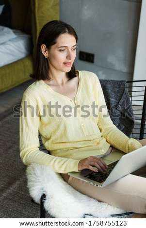Attractive young brunette woman using laptop computer while sitting in the bedroom