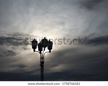 color photo with an old lantern against the sky and with the sun behind it