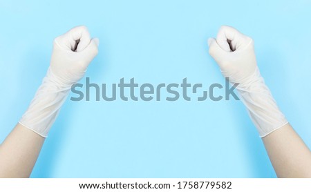 White latex medical gloves on a human's hand,stranglehold shows the gesture "keep fighting"for Medical staff isolated on blue background with copy space