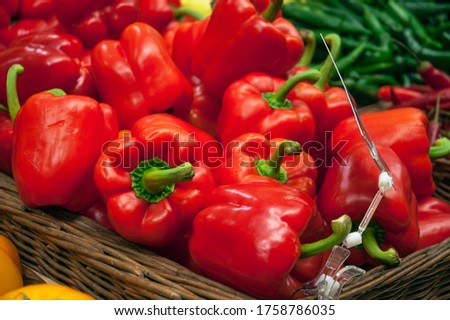 A bunch of ripe red peppers in a strong dark knitted box in the market and green chili peppers in the background