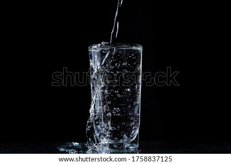 Water overflows the glass. Photo on a black background. Pure and purified water. Water pouring out of a glass Royalty-Free Stock Photo #1758837125