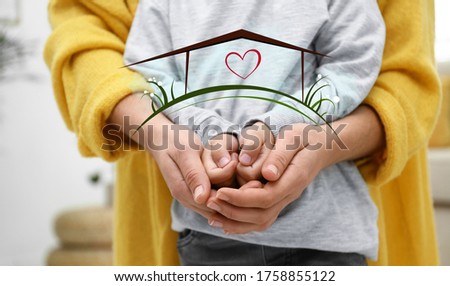 Mother holding hands with child and illustration of house indoors, closeup. Adoption concept