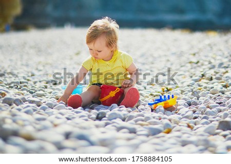 Adorable toddler girl playing with pebbles on the beach. Little child having fun near the sea in Etretat, Normandy, France. Outdoor activities for kids