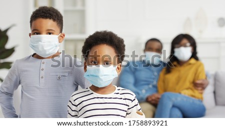 African American parents and cute small kids wearing protective masks at home. Stop the virus and epidemic diseases.