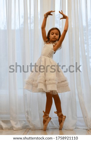 

girl ballerina in a white dress on pointe stands at the window