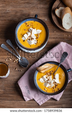 Pumpkin cream soup with cheese, crunchy croutons and pine nuts on a wooden table in warm colors top view.