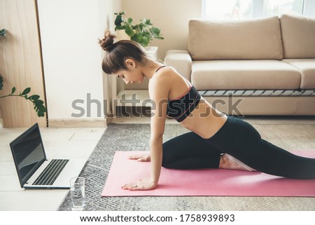 Side view photo of a caucasian woman doing fitness at home online using a laptop and glass with water on floor wearing sportswear