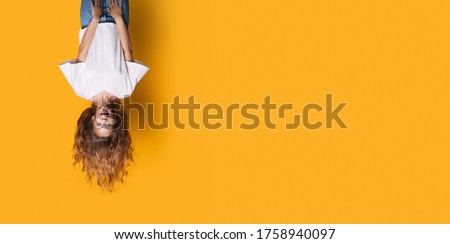 Upside down photo of a caucasian woman in white shirt and jeans smiling on a yellow studio wall with free space Royalty-Free Stock Photo #1758940097