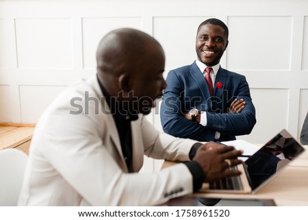 An African American in a white suit sitting at a laptop talks to an investor sitting next to him and explains to him the benefits of investing in his company Royalty-Free Stock Photo #1758961520