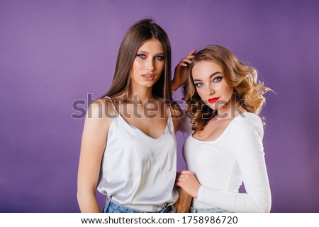 Two young and beautiful girls shows emotions and smiles in the Studio on a purple background. Girls for advertising