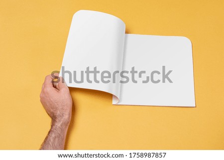 Male hand opened a catalog on yellow backdrop, editable mock-up series template ready for your design- pages selection path included