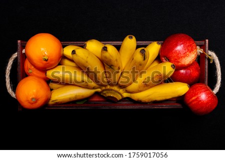 Natural fresh flat lay of banana, apples and lemons in a basket lay on a black background.