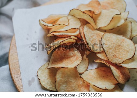 Fresh homemade deep fried crispy potato chips in white box on a wooden tray, top view. Salty crisps scattered on a table for a tasty snack break and party movie time.