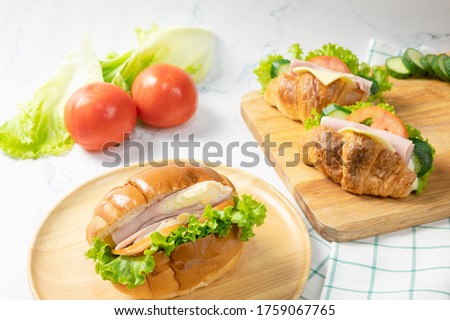Delicious croissants sandwichs with fresh Ham, cheese, tomato, cucumber, lettuce served on cutting board and Sub sandwich with fresh salad, Ham , cheese served on round wooden plate. white background.