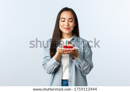 Social distancing lifestyle, covid-19 pandemic, celebrating holidays during coronavirus concept. Hopeful dreamy cute asian girl smiling pleased at birthday cake, making wish blowing bday candle