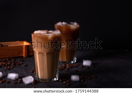 Iced coffee in a tall glass with cream poured over. Wood background. Low key