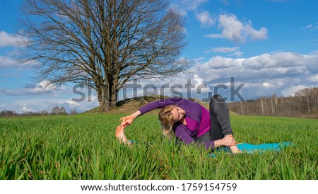 A middle-aged blonde woman in a tracksuit practices yoga outdoors. Healthy lifestyle and Slow life alone with nature. Taking care of yourself to stay healthy.