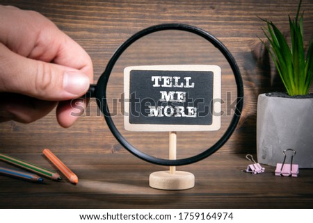 TELL ME MORE. Business, information, advice and solutions concept. Man's hand, holding magnifying glass Royalty-Free Stock Photo #1759164974