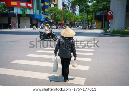 Vietnamese woman with conical hat walking on crosswalk in Hanoi