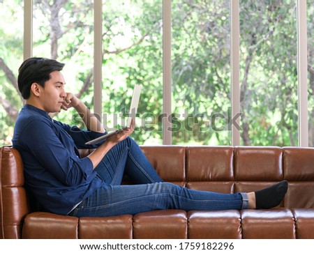Young man use laptop computer to search for jobs. Asian man spend holidays in the living room. 