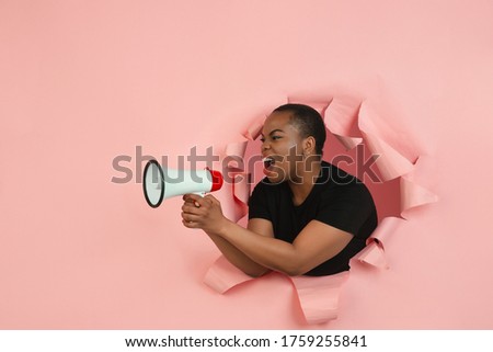 Shouting. Cheerful african-american young woman poses in torn coral paper background, emotional and expressive. Breaking on, breakthrought. Concept of human emotions, facial expression, sales, ad.