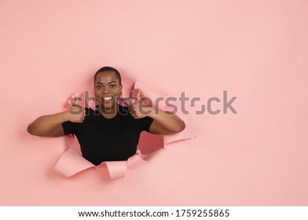 Thumbs up. Cheerful african-american young woman poses in torn coral paper background, emotional and expressive. Breaking on, breakthrought. Concept of human emotions, facial expression, sales, ad.