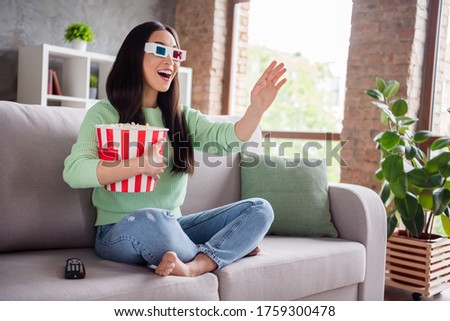 Full body profile side photo of surprised positive asian girl watch 3d film impressed modern effect hold pop corn box sit divan legs crossed bare foot in house indoors