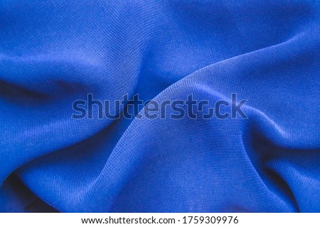 Close up picture of blue chiffon fabric with holds for fashion concept. Background with textured material and polyester structure. Macro photography of folded fabric for cloth design wallpaper.