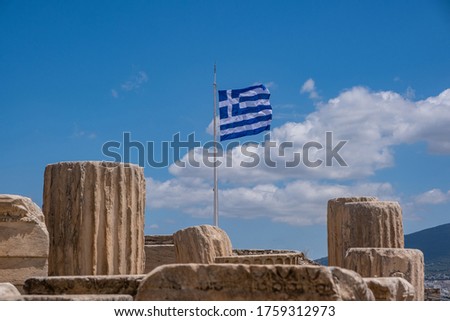 Athens Acropolis, Greece. Greek flag waving on pole, ancient column remains against blue sky background, spring sunny day.