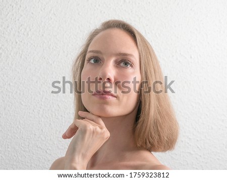 Portrait of beautiful middle aged woman touching her face on white wall. Beauty and skincare concept.