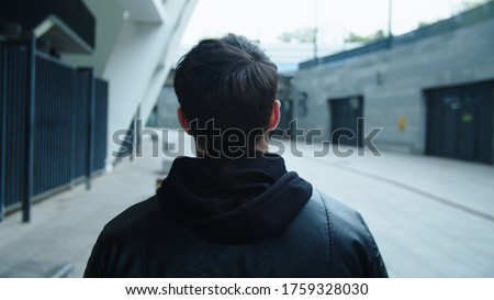 Back view of man walking on urban street in black jacket. Closeup young man walking on empty street in leather jacket. Man going on city street alone in slow motion. Royalty-Free Stock Photo #1759328030