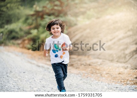 4-year-old brown boy running to the camera through a beautiful forest with green trees and yellow sunlight