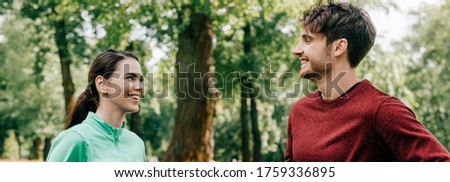 Panoramic crop of smiling sportswoman looking at boyfriend in park