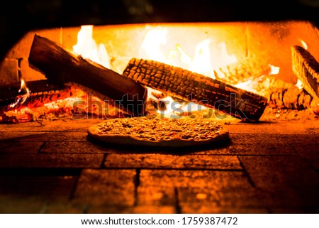 Pizza roasting in the oven with wood burning fire in the oven. Wooden firewood is burning in the stove