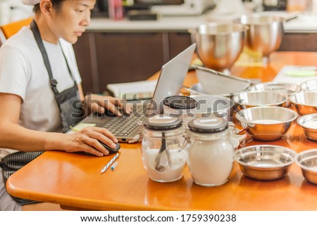 Female baker working on laptop with bakery ingredient on table Royalty-Free Stock Photo #1759390238