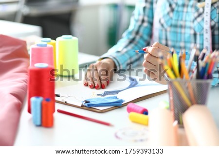 Woman designer draws sketch of fashionable dress close-up. On the table are spools of thread of different colors concept.
