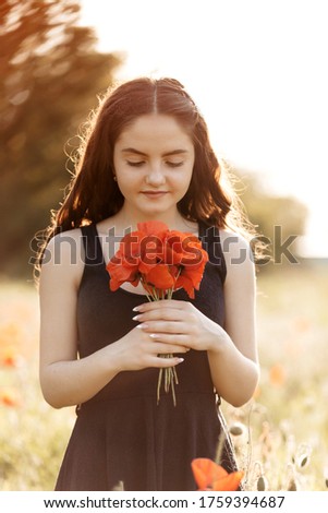 Beautiful, young woman with a bouquet of poppies in a sunset poppy field