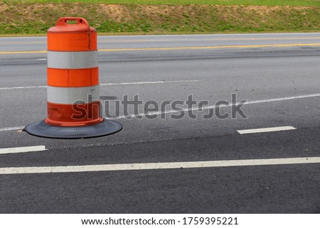 Orange and white striped traffic safety barrel on an asphalt street, road construction zone, horizontal aspect