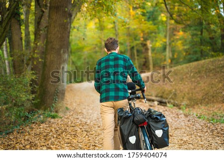 Hipster man pushing a bicycle at a public park during autumn.