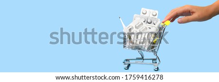 Side view of a woman hand pushing and rolling a mini shopping cart full of pills. The concept of online shopping medicine on blue background. Online Pharmacy. health insurance. Banner. Space for text Royalty-Free Stock Photo #1759416278