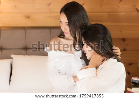 Two women in white shirt pajamas sit talk together.relax in bed on holiday.