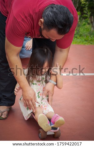 Adult pushing toddler on skateboard in the park. Learning and family concept.
