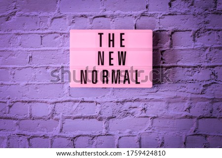 THE NEW NORMAL sign hanging on wall in neon colors. Pink signboard THE NEW NORMAL in on vintage purple brick wall background in fluorescent light. Changed lifestyle and rules concept